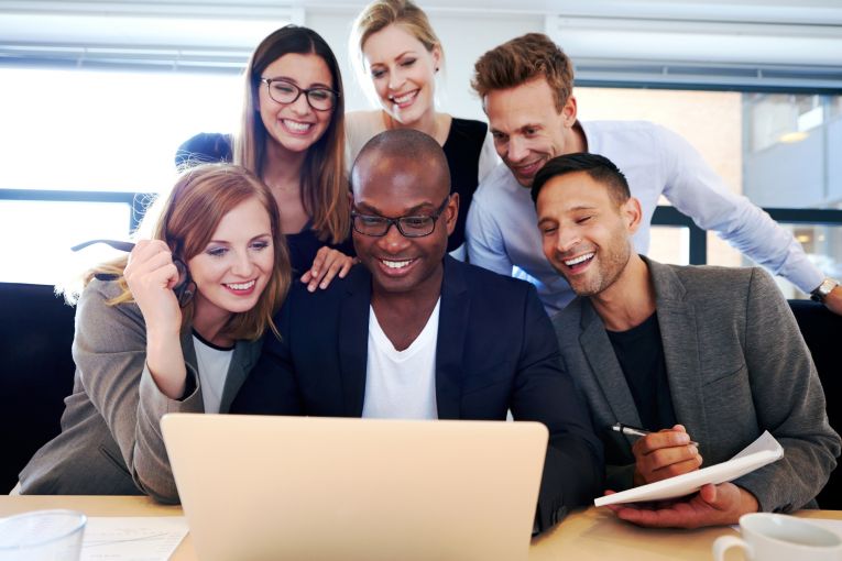 Group of young professionals smiling in front of a laptop